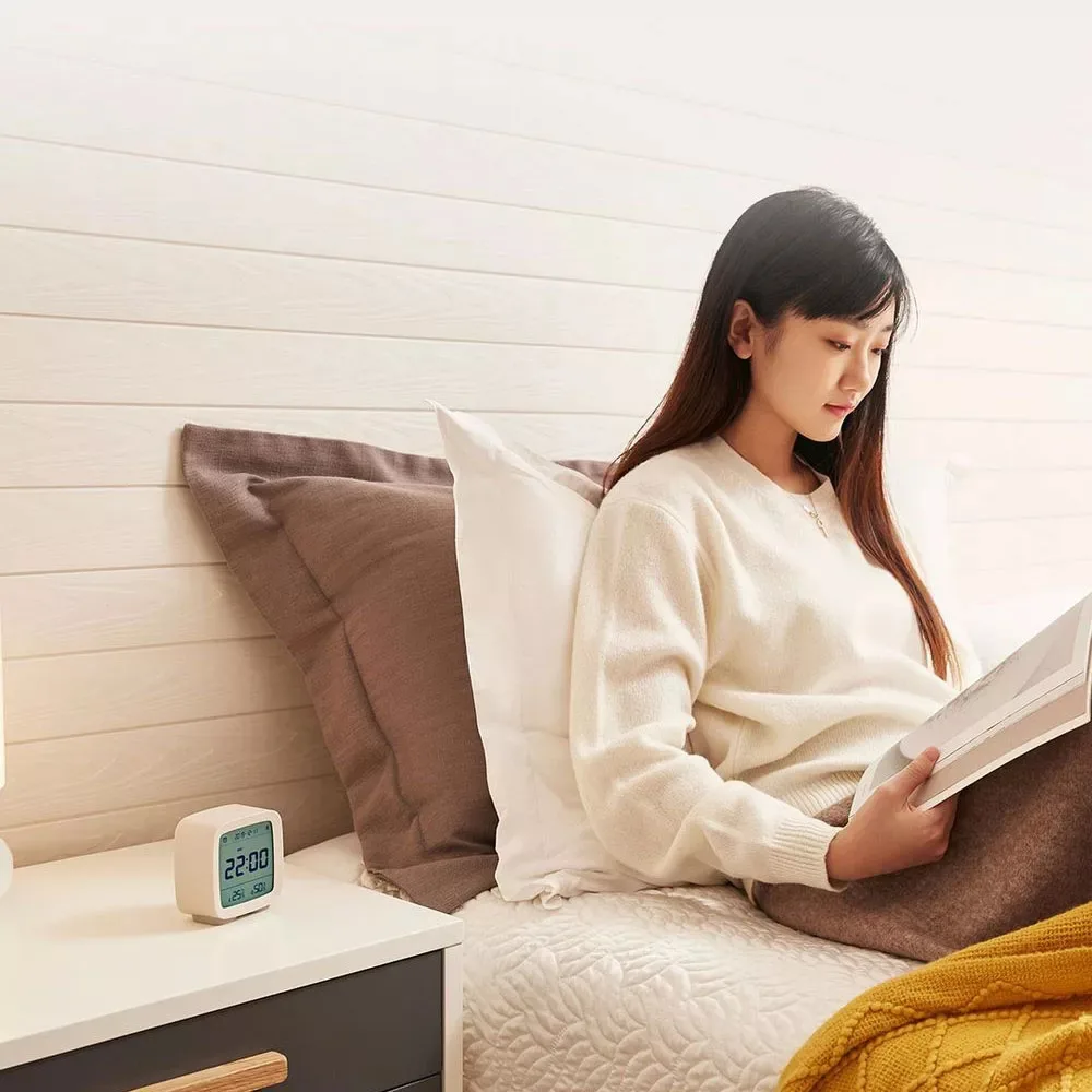 Réveil thermo-hygromètre sur une table de chevet, une femme lit au lit