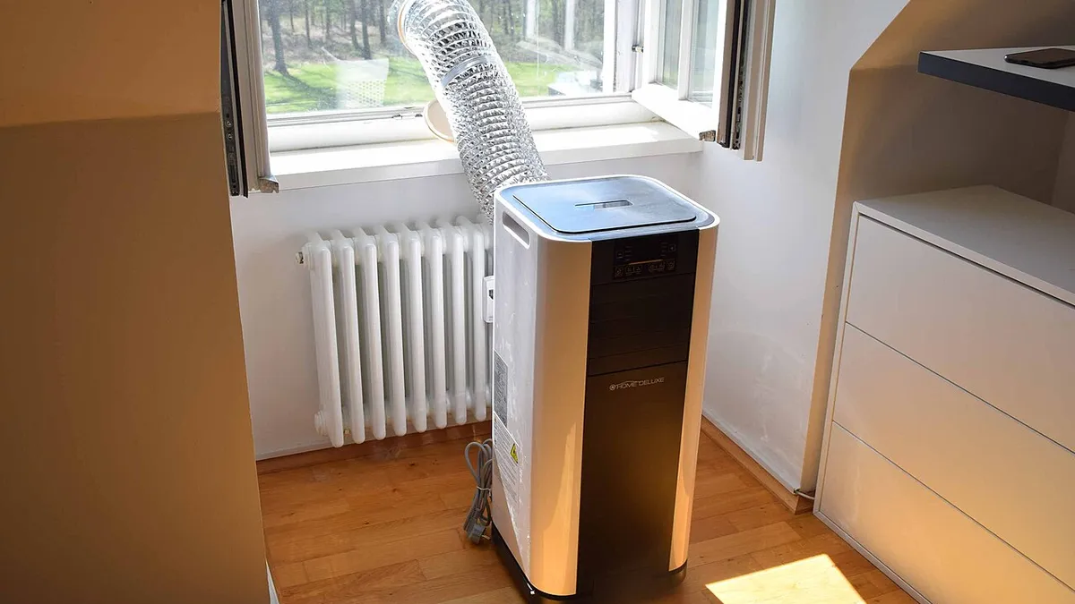 Climatiseur mobile posé près d’une fenêtre, gaine d’évacuation passée par l’ouvrant